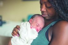 African American mom gently cradles her newborn daughter against her chest.